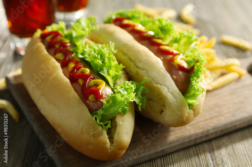 Delicious hot-dogs with French fries on wooden chopping board, close up