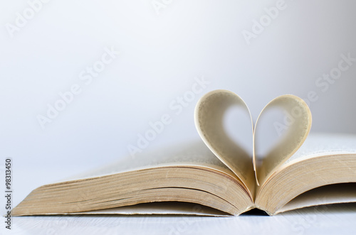Open old book on a table with pages in a heart shape and neutral background