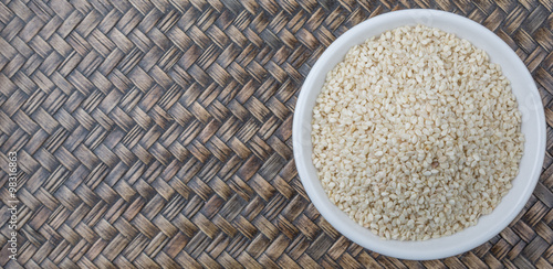 White sesame seed in white bowl over wooden background