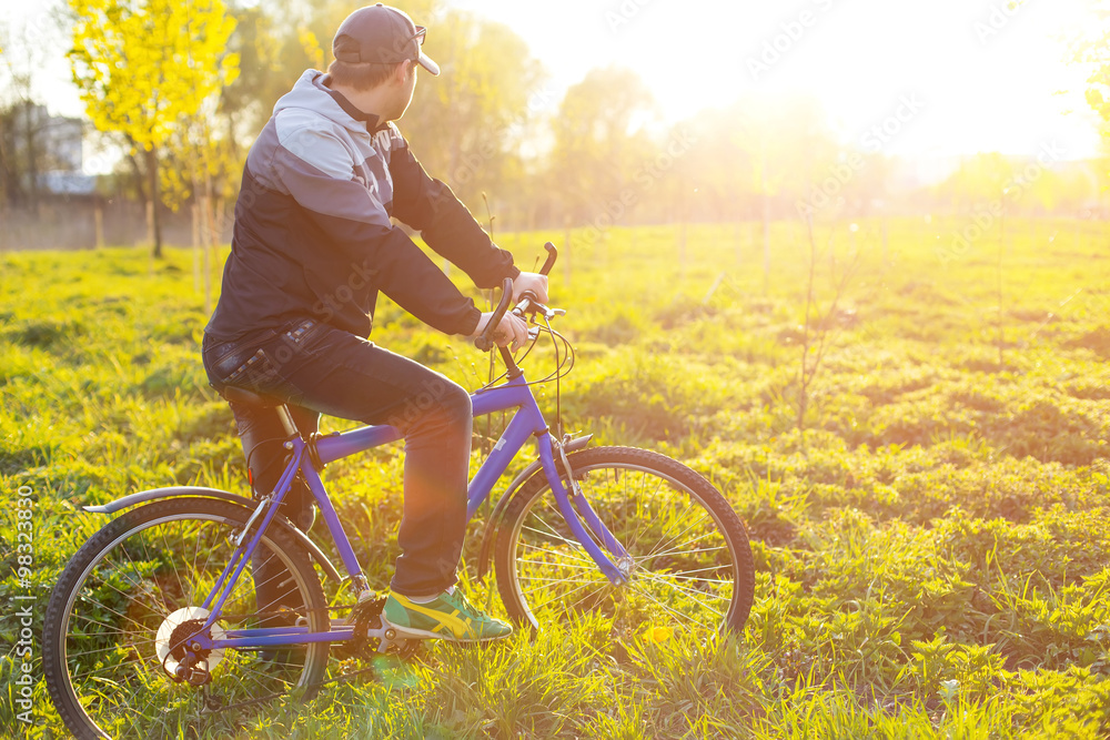 Obraz premium Young man cycling on a rural road through green spring meadow du
