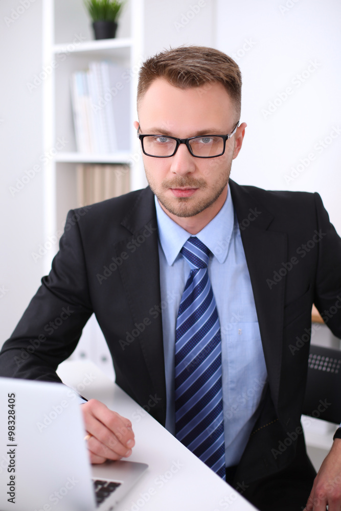 Portrait of young business man sitting at the desk on office background. Portrait of young business man sitting at the desk on office background.