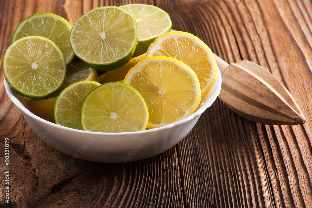 Heap of whole and sliced lemons and limes and citrus reamer over wooden background. Top view Heap of whole and sliced lemons and limes and citrus reamer over wooden background. Top view
