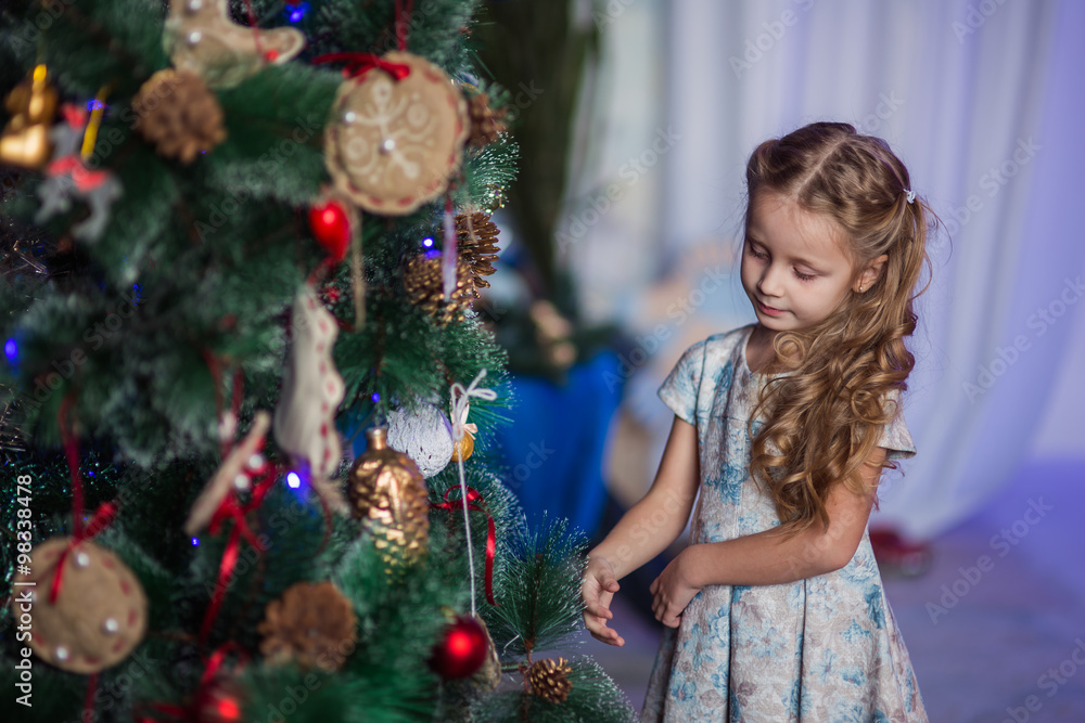 Радостная девочка украшает елку игрушками к новому году