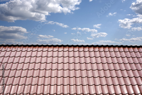 Gable roof of a house covered with metal tile closeup against blue sky with white clouds