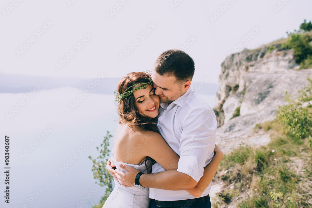 a happy married couple posing on the rock near the lake