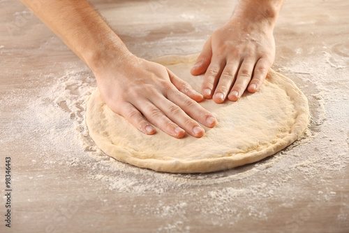 Foto Hands preparing dough basis for pizza on the wooden table, close-up