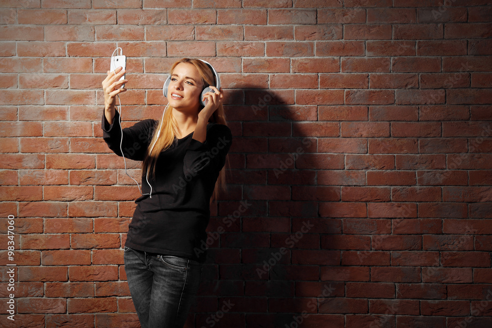 Young woman standing at the brick wall and listening to music Young woman standing at the brick wall and listening to music