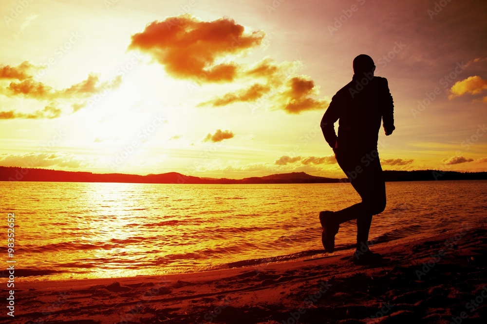 Silhouette of sport active man running and exercising on beach at vivid colorful sunset.