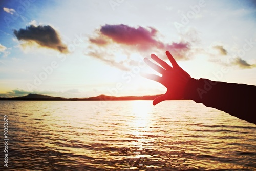 Silhouette of hand and lomg fingers try to touch the sun,  sunset above ocean . Vivid colors. photo