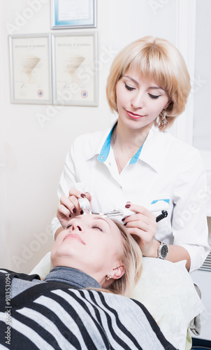 beautiful girl beautician making permanent makeup on woman's face. Blonde. doctor.