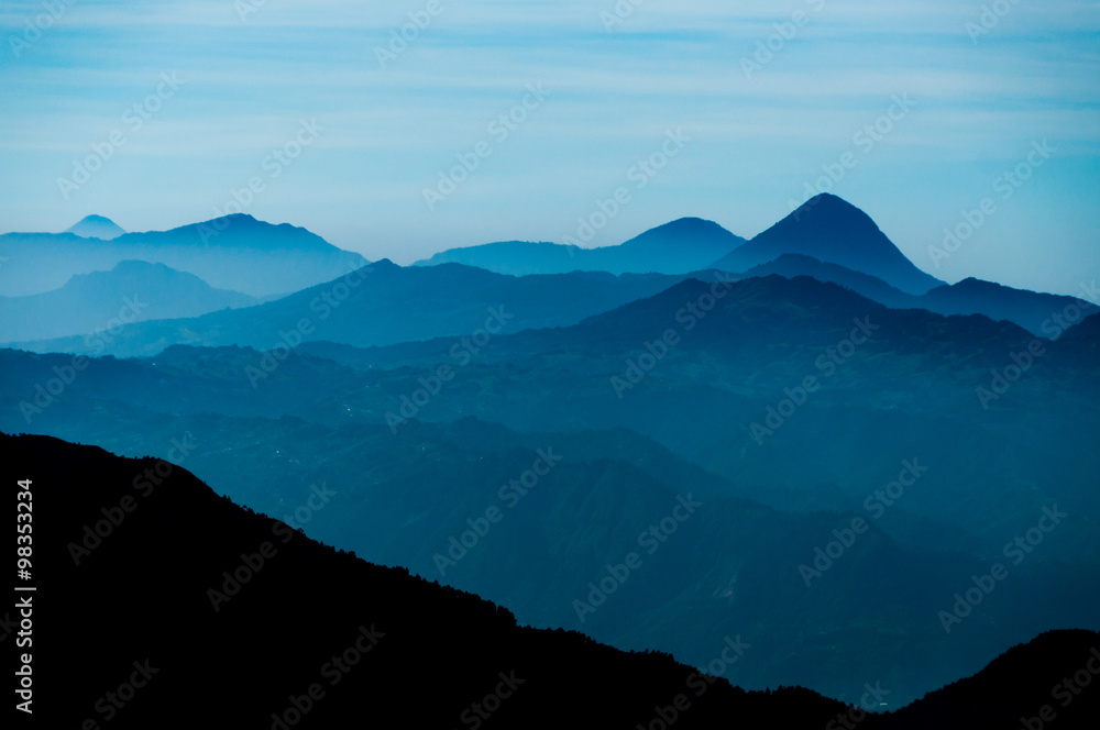 Obraz premium Black Mountain Silhouette in front of Skyscape cold blue mountains with mist and fog close to Quetzaltenango