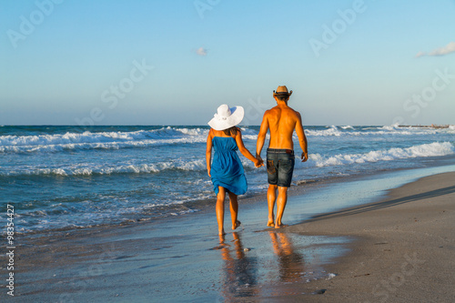 Young couple walking barefoot on a wet beach at dusk.