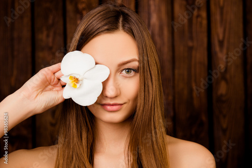 Portrait of pretty girl holding an orchid near her eyes