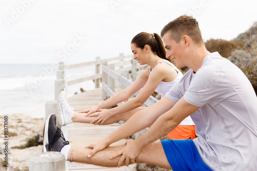 Runners. Young couple exercising and stertching on beach