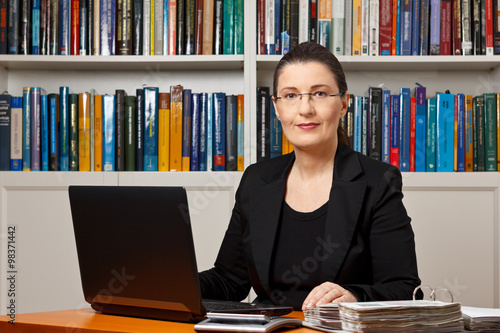 Mature woman in an office or library with laptop, calculator and files binder, tax or financial accountant, consultant, adviser or counselor. photo