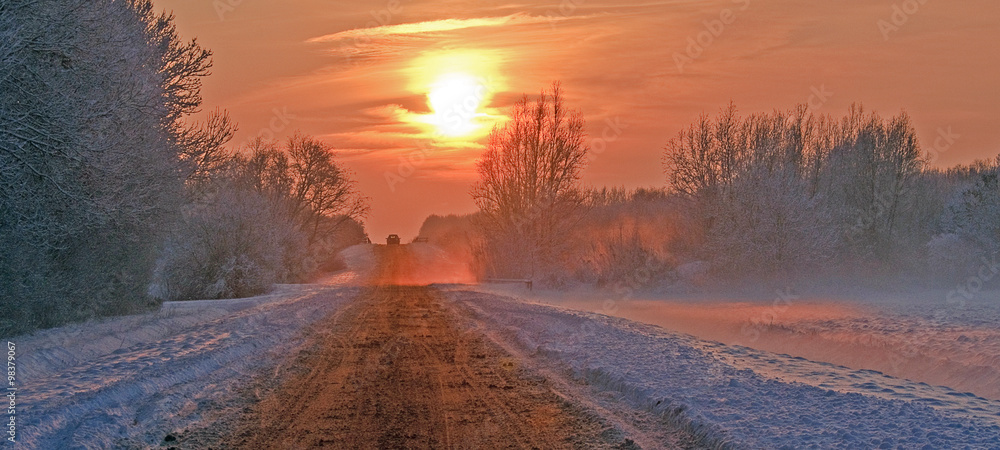 Snowy road through the countryside at sunset
