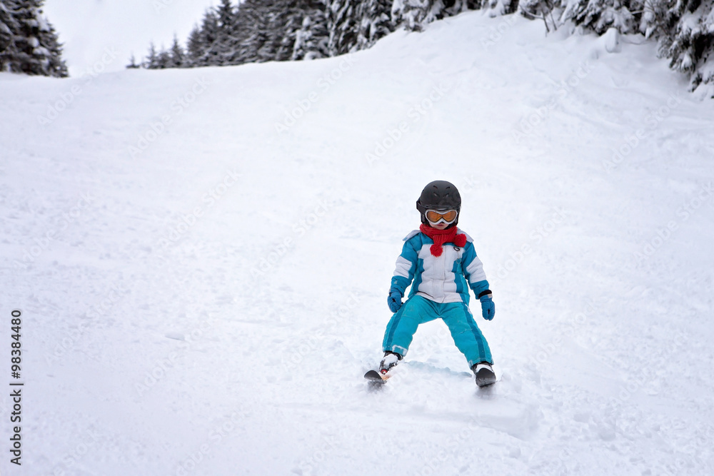 Adorable little boy with blue jacket and a helmet, skiing wintertime
