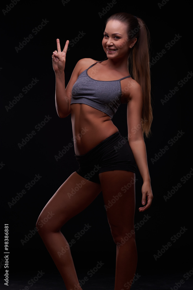 Fototapeta premium Beautiful young girl on a dark background is engaged in fitness