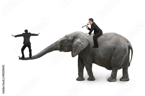 One man using speaker riding elephant another balancing on trunk