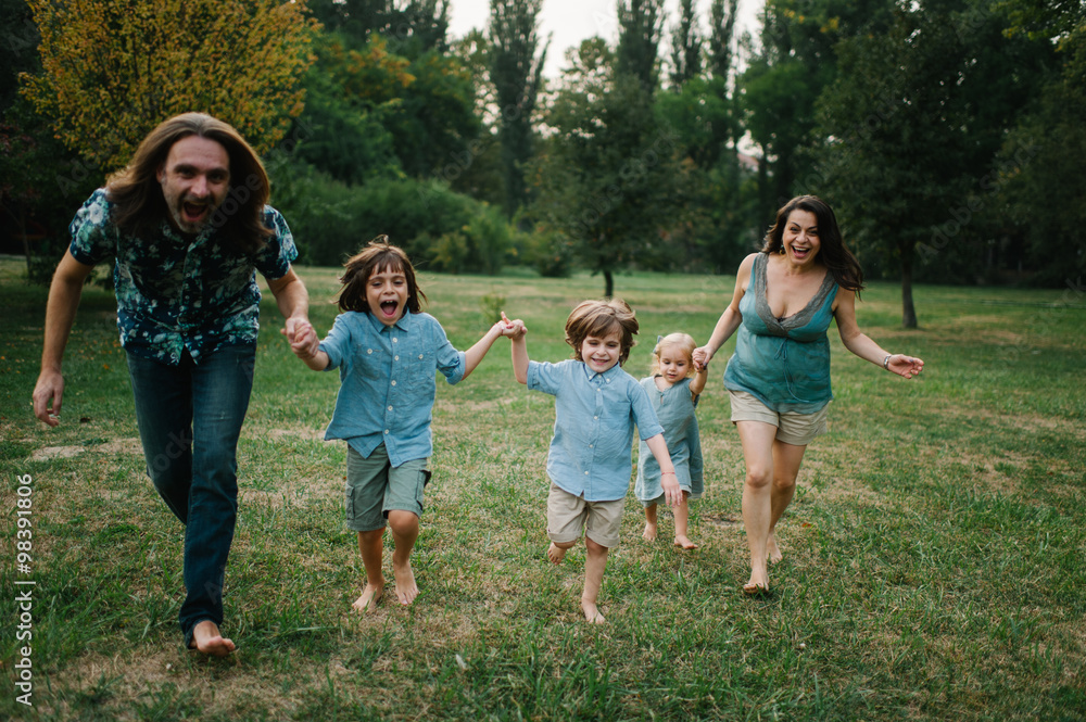 Fototapeta premium Happy young hipster family having fun while running, bowl, rising up, piggyback ride their children in park on summer sunset 