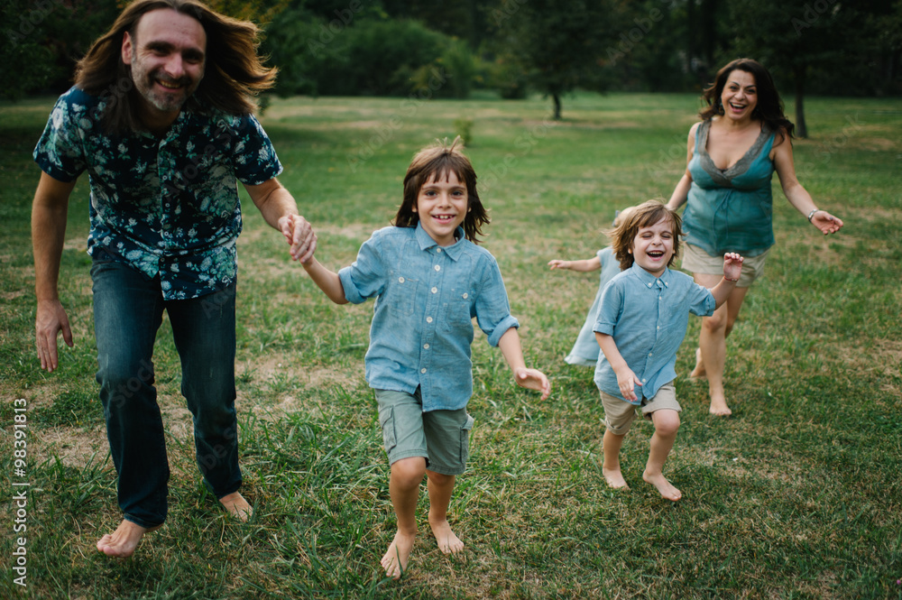 Obraz premium Happy young hipster family having fun while running, bowl, rising up, piggyback ride their children in park on summer sunset 