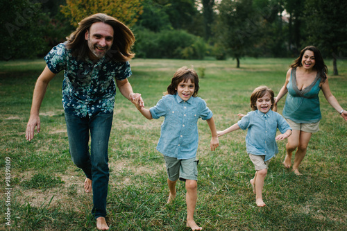 Happy young hipster family having fun while running, bowl, rising up, piggyback ride their children in park on summer sunset 