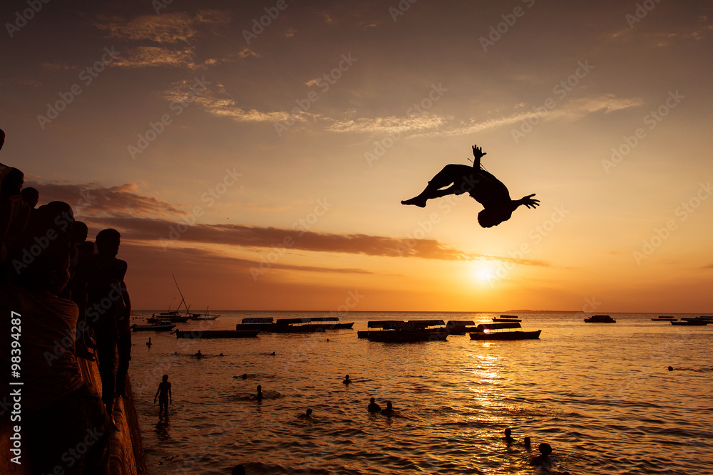 Silhouette of Happy Young boy jumping in water at sunset in Zanz - obrazy, fototapety, plakaty 