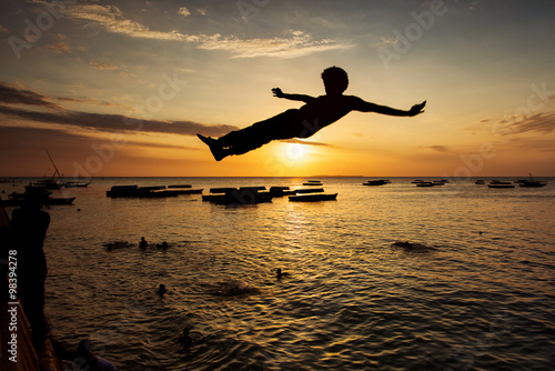 Silhouette of Happy Young boy jumping in water at sunset in Zanz