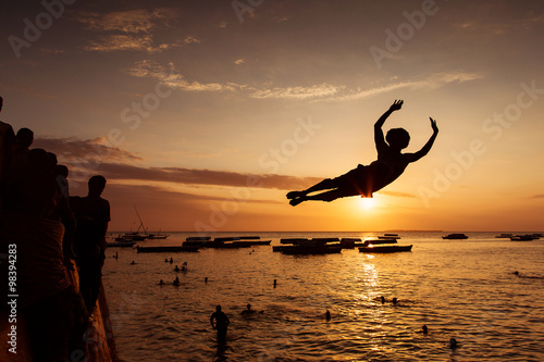 Silhouette of Happy Young boy jumping in water at sunset in Zanz