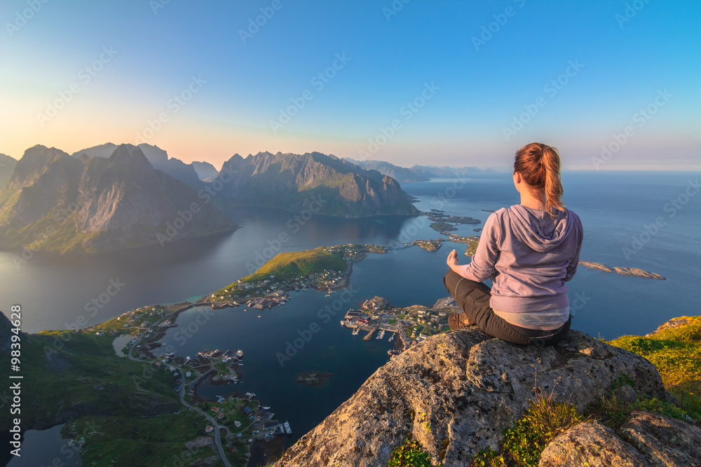 Young beautiful concentrated woman doing yoga exerices on top of the mountain enjoying the breathtaking view over blue lagoon, green islands,small village and sunset Young beautiful concentrated woman doing yoga exerices on top of the mountain enjoying the breathtaking view over blue lagoon, green islands,small village and sunset
