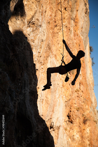 Silhouette of rock climber hanging on belay rope againstthe mountains