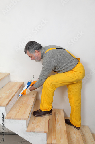 Construction worker caulking wooden stairs with silicone glue using cartridge
