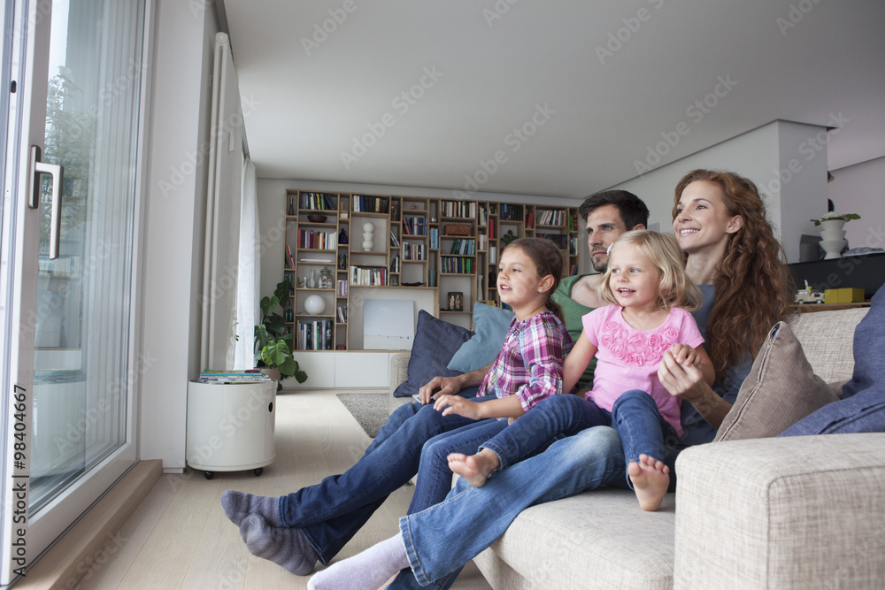 Couple and two little girls sitting on couch in the living room looking through terrace door Couple and two little girls sitting on couch in the living room looking through terrace door