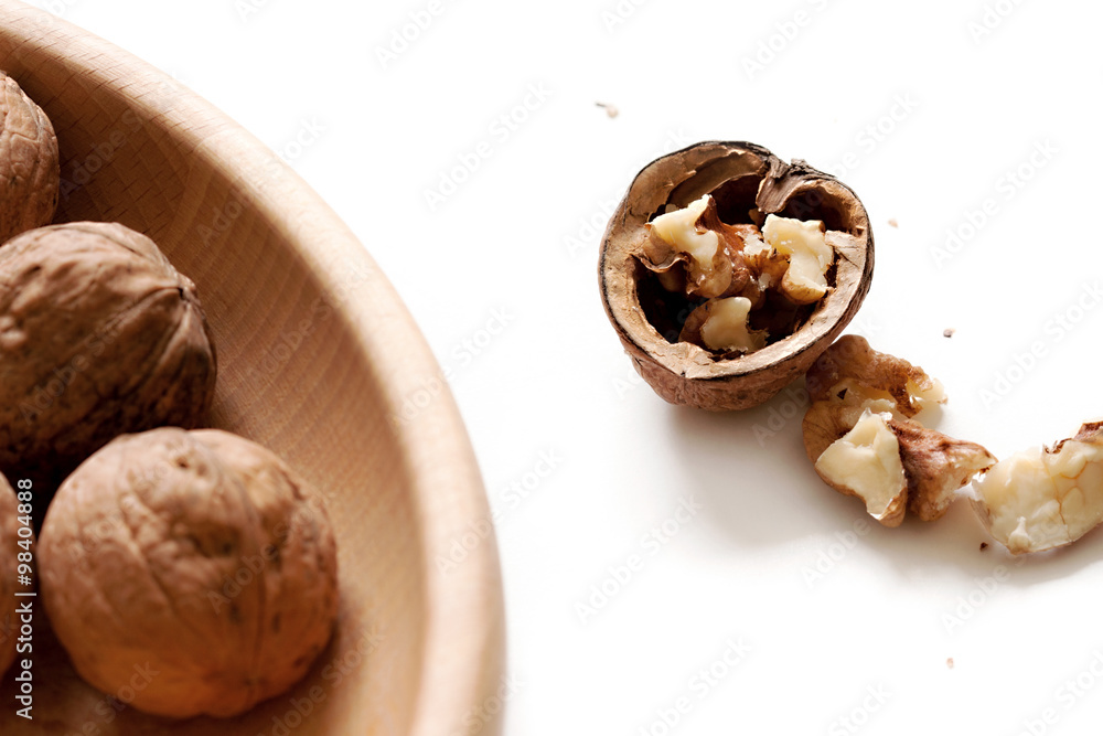 Single cracked open half walnut and several full walnuts on plate, white isolated background Single cracked open half walnut and several full walnuts on plate, white isolated background