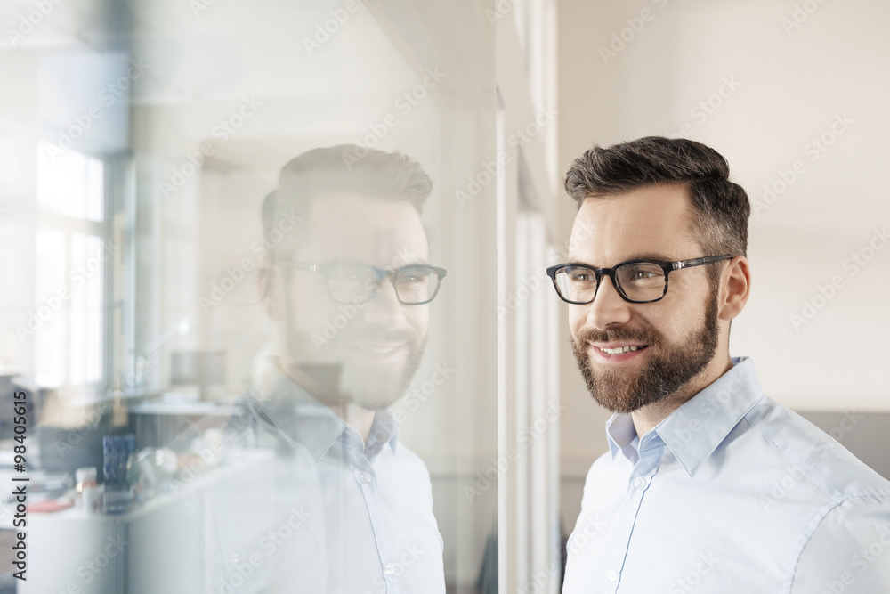 Smiling businessman looking through glass wall Smiling businessman looking through glass wall