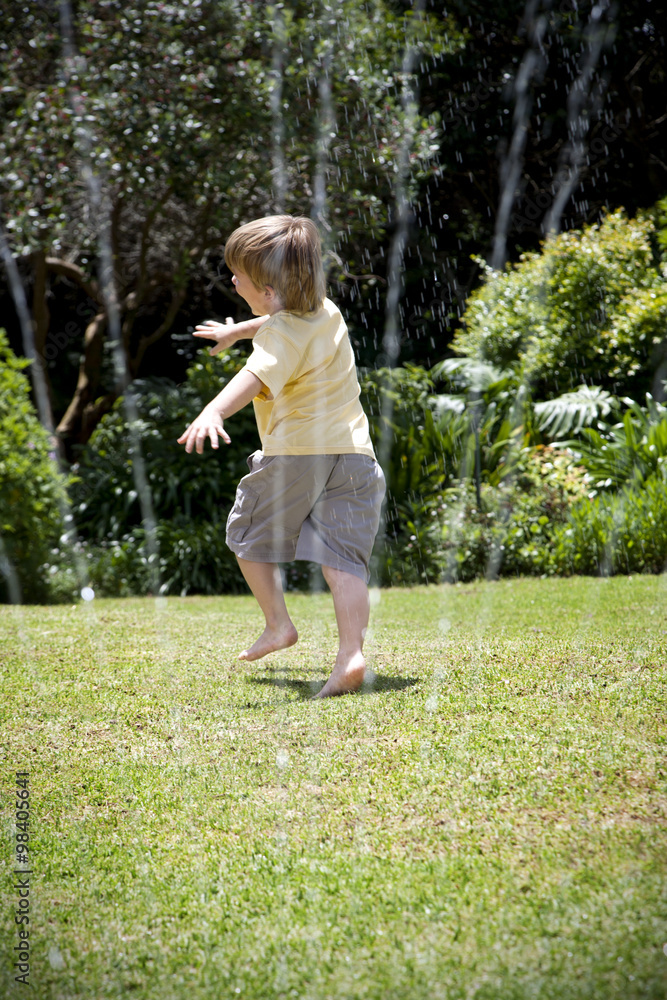 Little boy playing with lawn sprinkler in the garden Little boy playing with lawn sprinkler in the garden