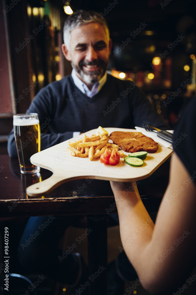 Smiling man in restaurant receiving Wiener Schnitzel with French fries Smiling man in restaurant receiving Wiener Schnitzel with French fries