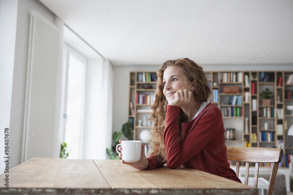 Smiling woman at home sitting at wooden table with cup Smiling woman at home sitting at wooden table with cup