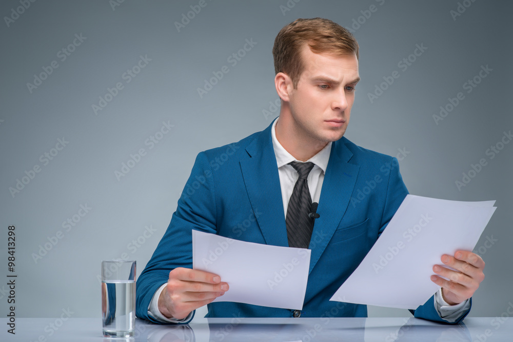 Serious-looking newscaster reading his papers. Serious-looking newscaster reading his papers.