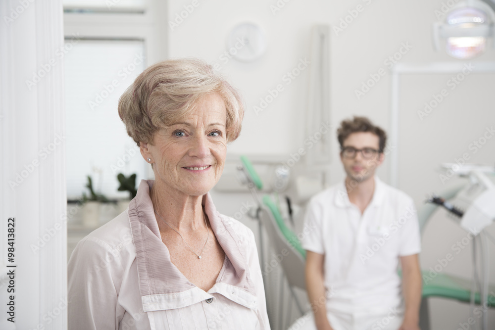Portrait of smiling senior woman in surgery with dentist in background Portrait of smiling senior woman in surgery with dentist in background