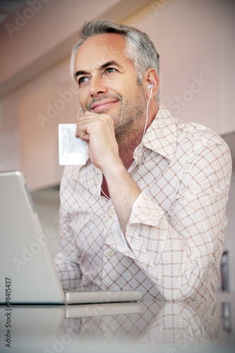 Portrait of smiling man with earphones and laptop holding credit card