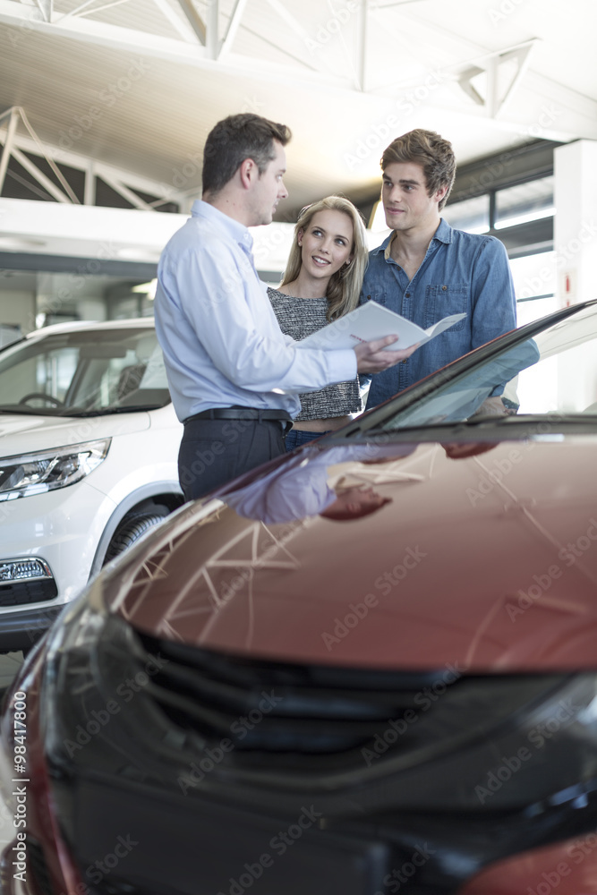 Car dealer showing brochure to young couple in showroom Car dealer showing brochure to young couple in showroom
