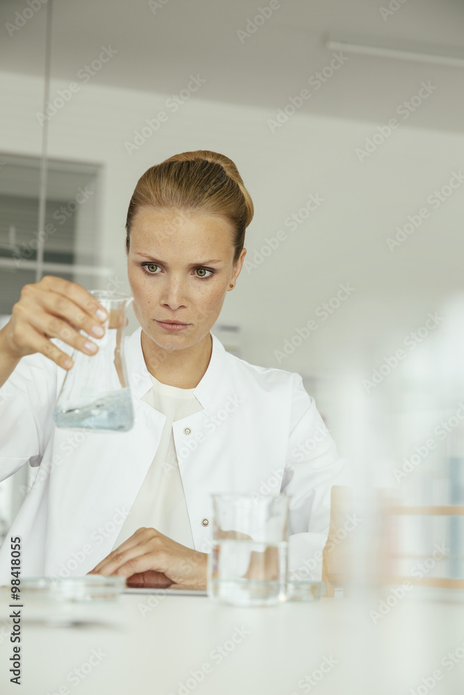 Female scientist looking at beaker with liquid Female scientist looking at beaker with liquid