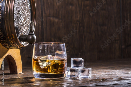 Принти на полотні Copper forged barrel and a glass of whiskey and ice on a old tab