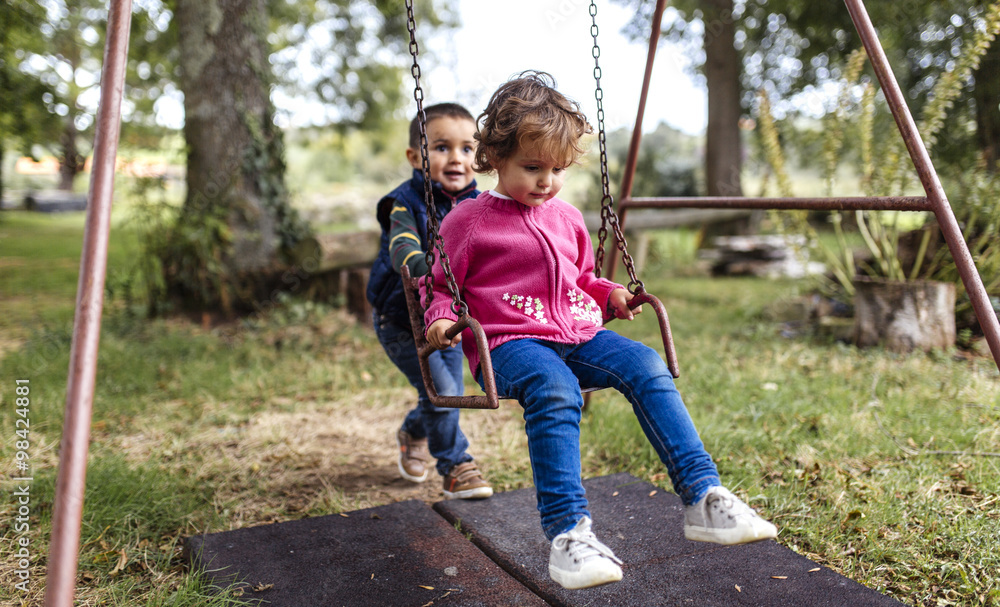 Two little children playing with swing in a garden Two little children playing with swing in a garden