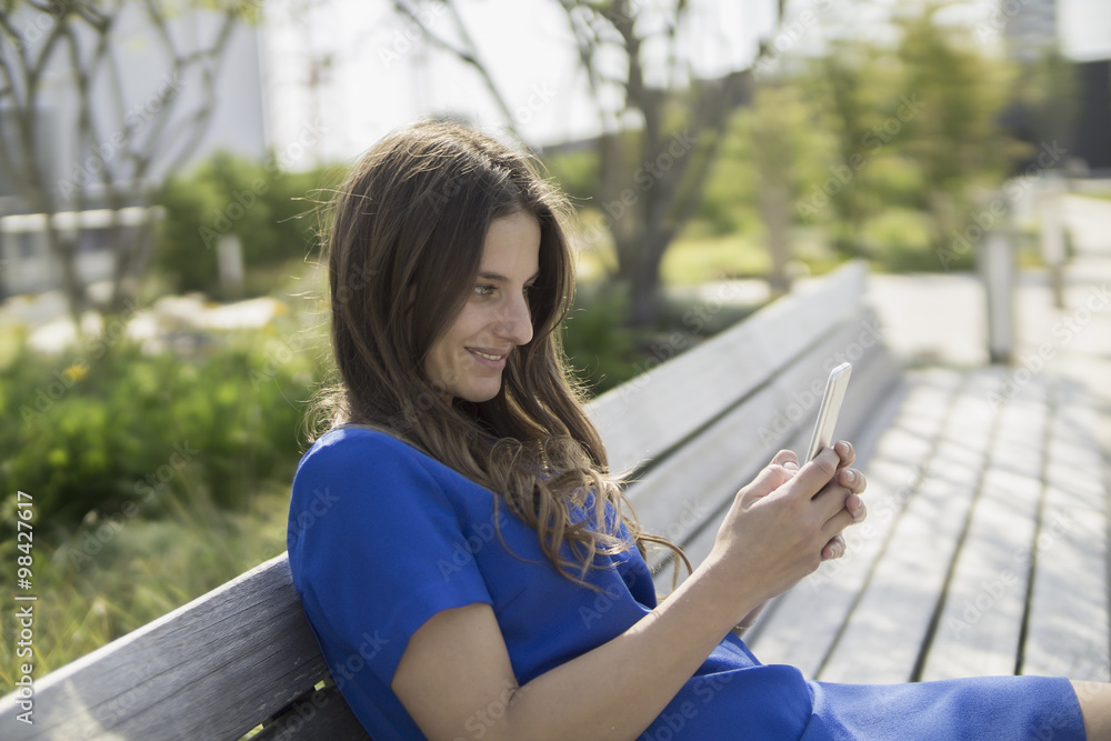 Smiling businesswoman sitting on a bench looking at smartphone Smiling businesswoman sitting on a bench looking at smartphone