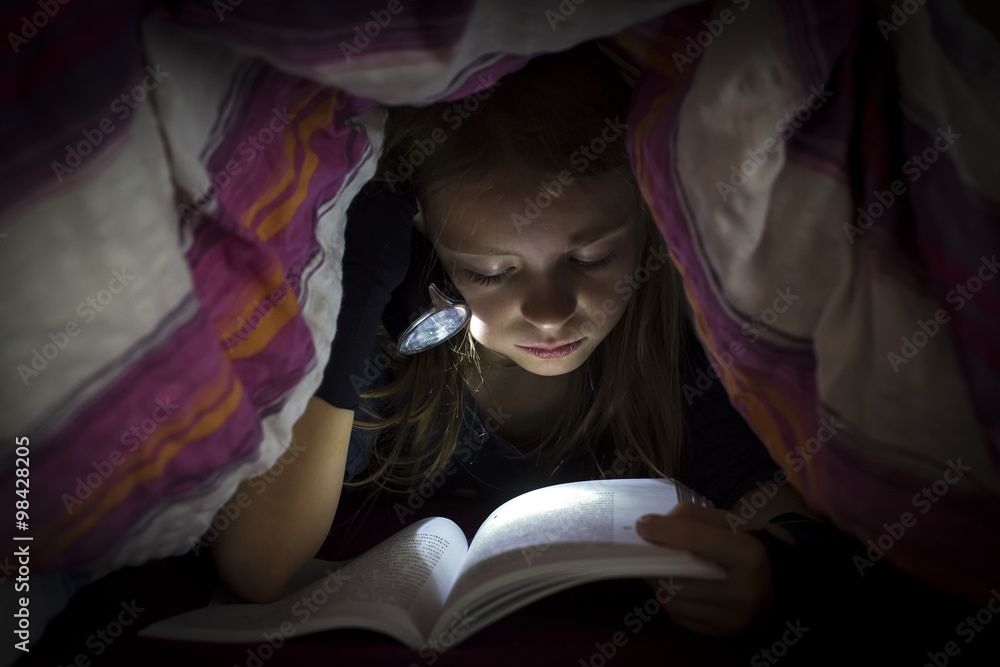 Little girl with torch reading book under a blanket Little girl with torch reading book under a blanket