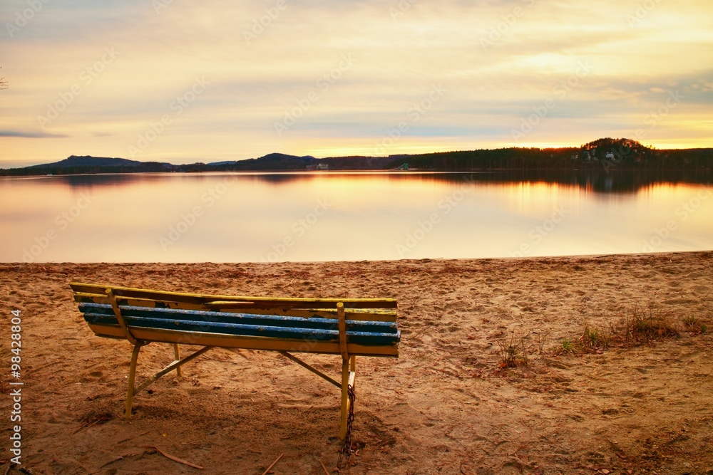 Outdoor empty bench on autumn lake beach. The coast with shining sun. Vintage toned photo