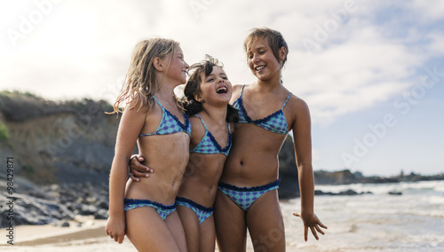 Three girls standing arm in arm on beach having fun photo