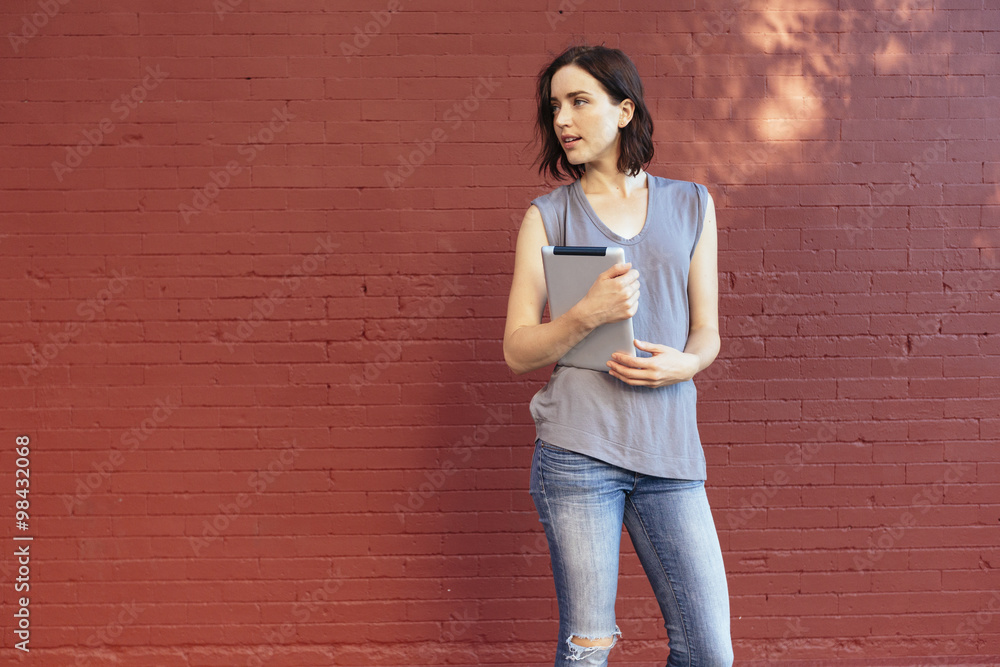 Portrait of woman with digital tablet standing in front of red brick wall Portrait of woman with digital tablet standing in front of red brick wall